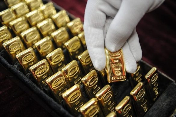 Une main gantée de blanc sélectionne avec soin un lingot de l'or pur parmi une collection de lingots russes estampillés de 100g.