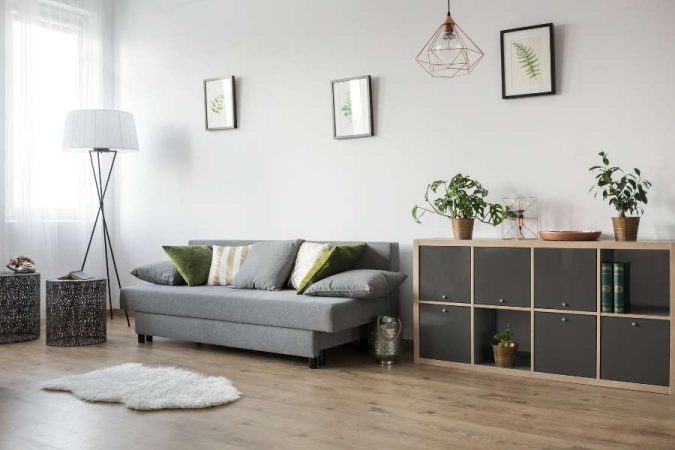 Un salon contemporain optimisé avec des meubles multifonctions, incluant un canapé gris convertible et un meuble de rangement modulaire.
