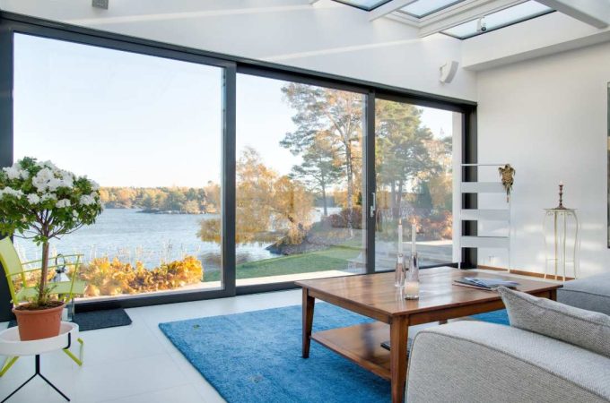Grand salon lumineux avec de larges baies vitrées offrant une vue sur un lac, un atout majeur parmi les critères évaluation valeur bien immobilier.