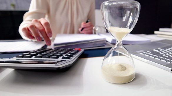 Femme calculant l'investissement et le temps (sablier) sur son bureau, évoquant la gestion de portefeuille de métaux précieux.
