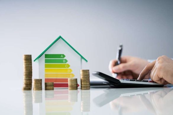 Une maquette de maison affichant une échelle de performance énergétique colorée de A à E, entourée de pièces de monnaie empilées, symbolisant les enjeux financiers du diagnostic énergétique.