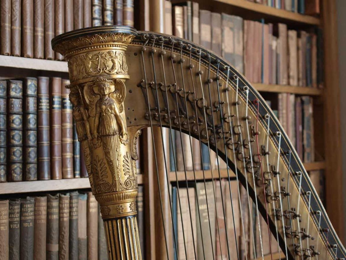 Gros plan sur la partie supérieure d'une harpe dorée sculptée, avec ses cordes, devant une bibliothèque ancienne floue.