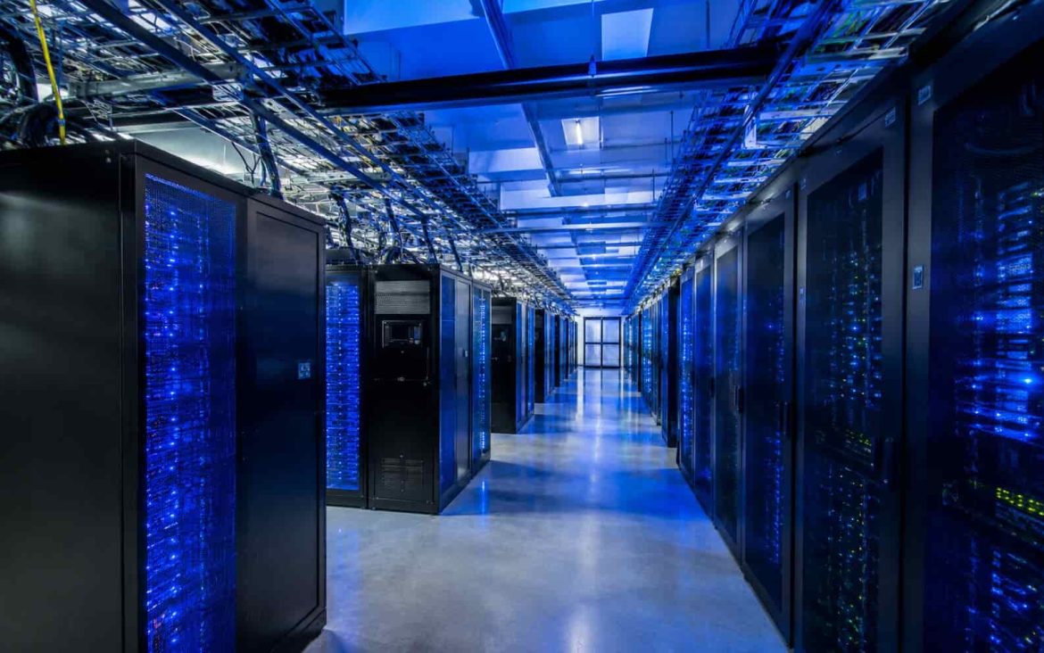 Allée de serveurs informatiques modernes dans un centre de données éclairé en bleu, illustrant la puissance de calcul nécessaire alors que l’intelligence artificielle ouvre une nouvelle bataille industrielle mondiale. Titre : Serveurs de centre de données : au cœur de l’IA.