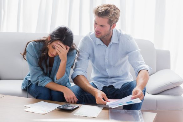 Un couple assis sur un canapé, l'homme regarde des papiers d'un air inquiet et la femme se tient la tête, illustrant une discussion difficile lors d'un processus de divorce.