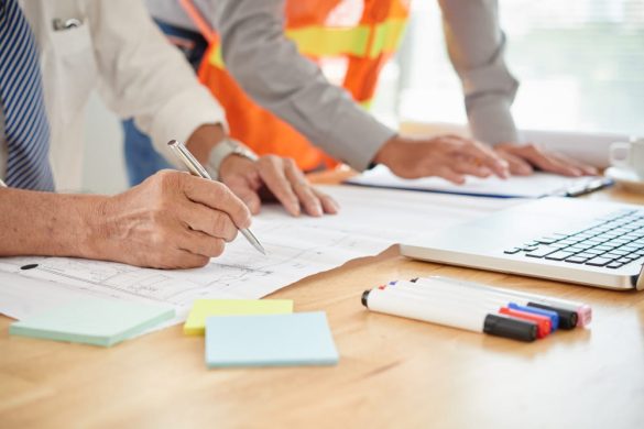 Deux collaborateurs, dont un en gilet de sécurité, analysent et annotent une grille inspection CSE sur un plan détaillé.