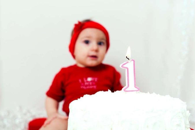 Un bébé habillé en rouge célèbre son premier anniversaire mémorable avec un gâteau et une bougie.