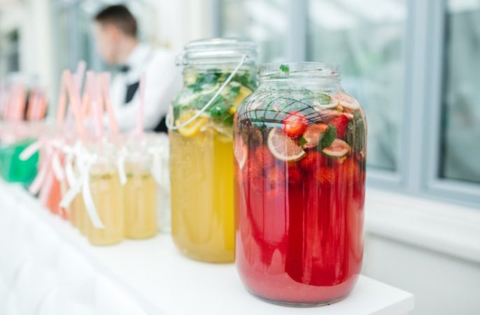 Grandes jarres en verre garnies de fruits frais et boissons colorées, une idée bar à boisson original pour mariage.