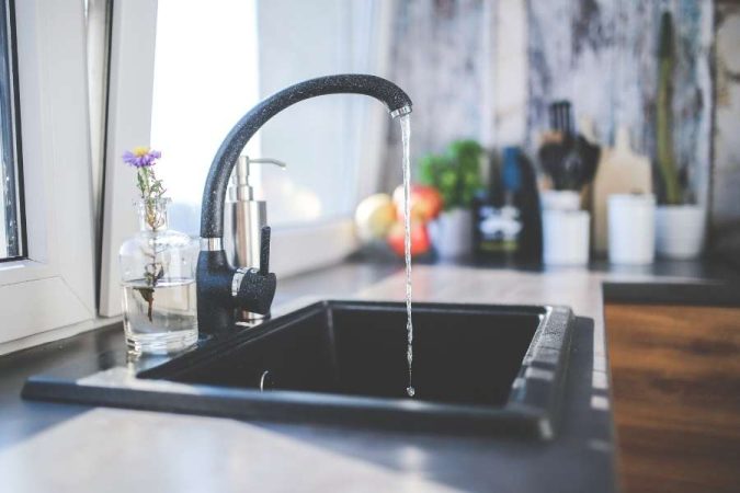 Un robinet mitigeur de cuisine noir à bec haut coule au-dessus d'un évier encastré, dans une cuisine moderne lumineuse.