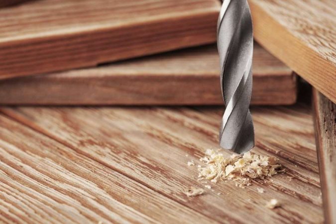 Un foret de perceuse en action posé sur un plateau en bois d'un établi pliant.